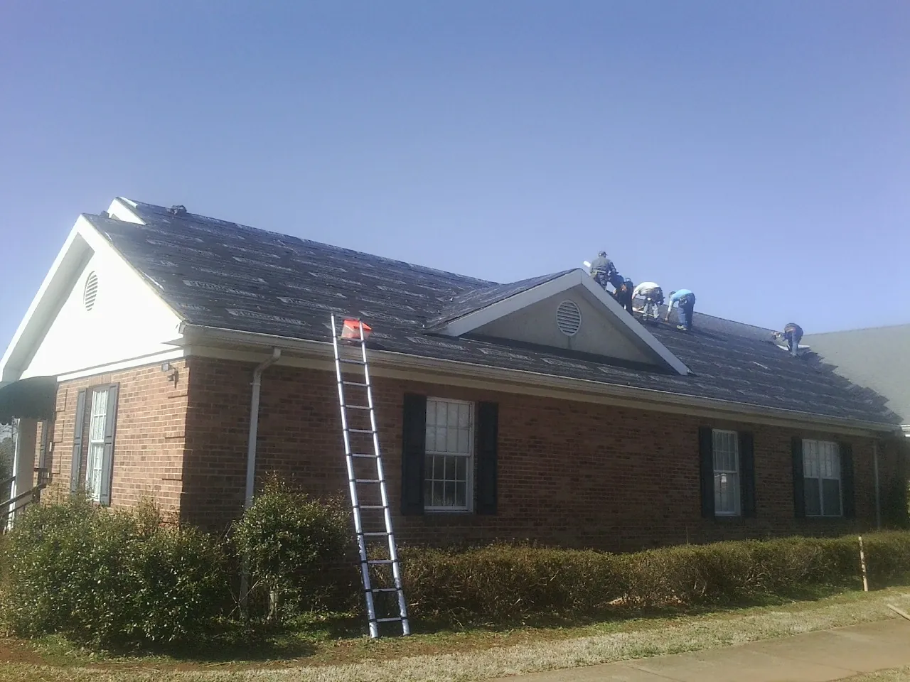 Crew tearing shingles off a brick ranch roof with a ladder set — Metal Roof Repair work by our crew in Poestenkill