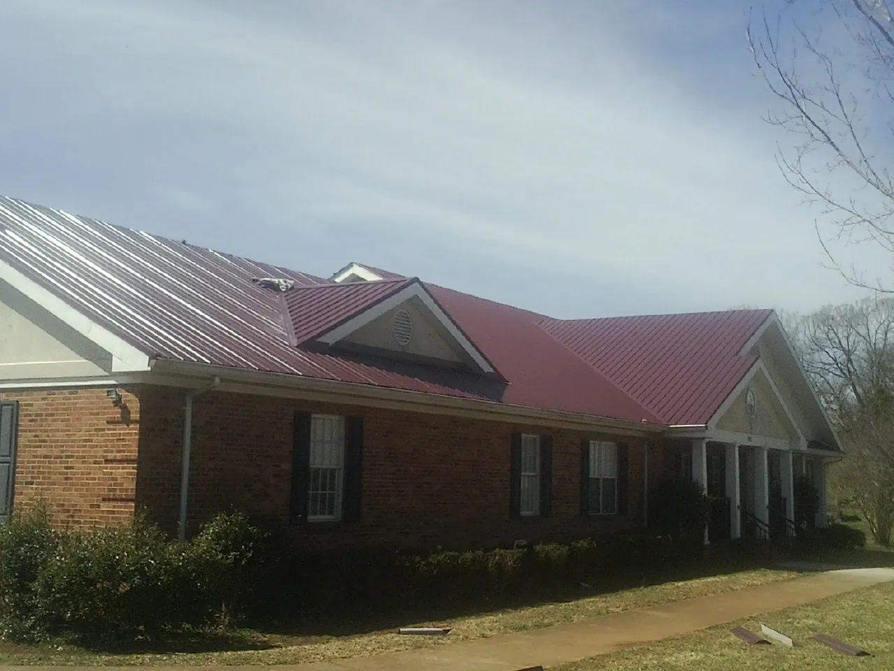 Red metal roof with gabled entries on a long brick building, from a Hail Damage Roof Repair job in Poestenkill