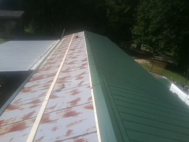 Old rusted panels beside newly installed green metal roofing — Wind Damage Roof Repair by Roofing Brothers in Poestenkill