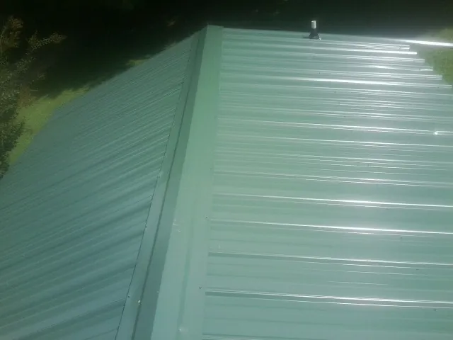 New green metal panels meeting at the ridge of a roof — Flat Roof Repair work by our crew in Poestenkill