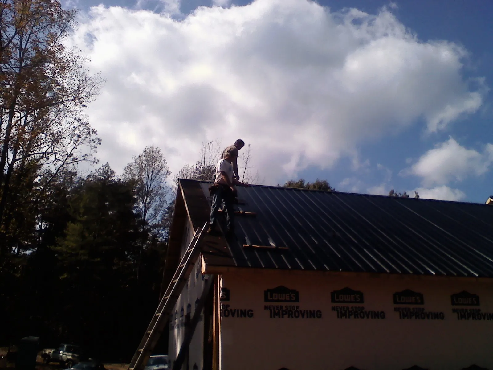 Roofer fastening dark metal panels high against a cloudy sky, from a Roof Inspection job in Poestenkill