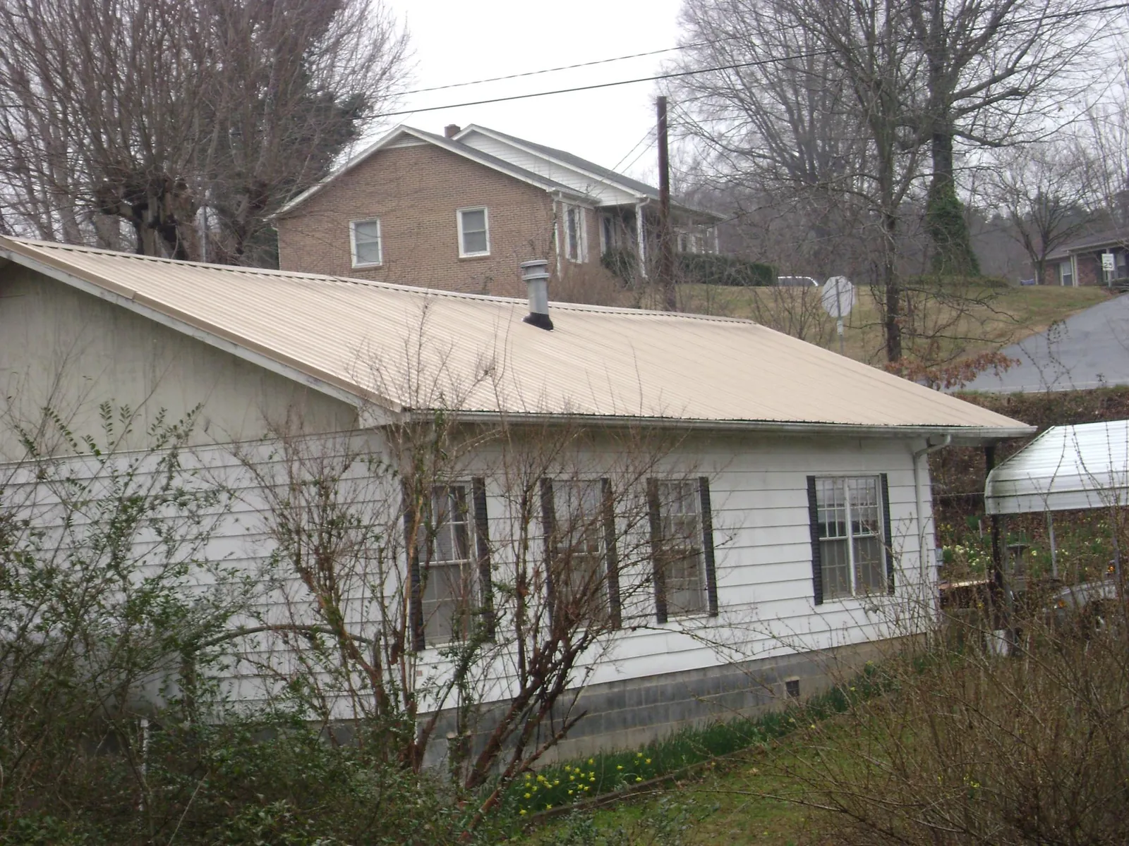 Tan metal roof on a white sided house set into a hillside — Commercial Roofing by Roofing Brothers in Poestenkill